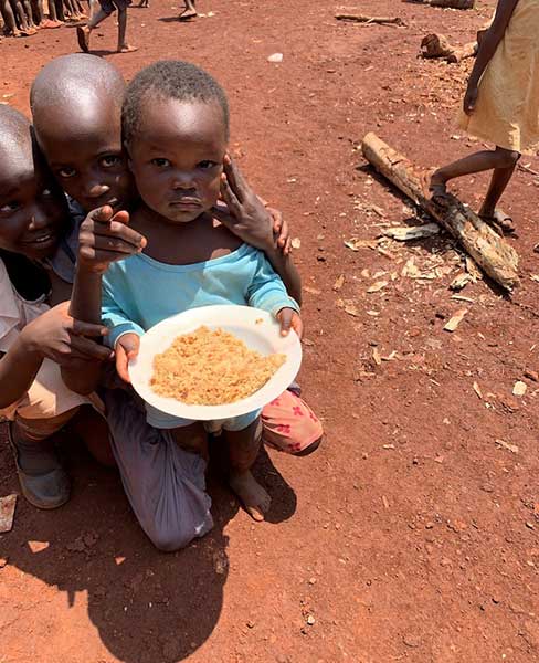 A photo of a young African girl holding a bowl of food and looking up at the camera.