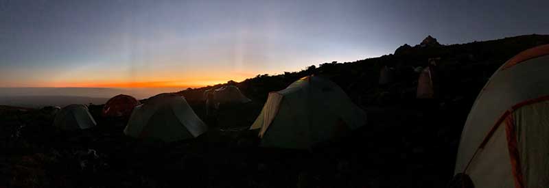 A photo of the Man Up and Go group's tents camped on the side of Mt. Kilimanjaro with a beautiful sunset in the background.