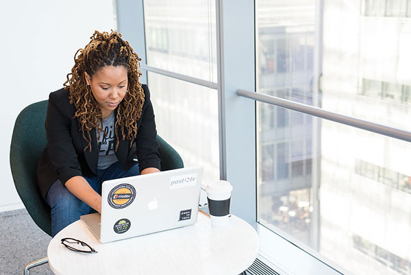 Image of a Black woman working on a laptop in an office building.