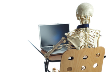 A skeleton sits at a desk typing on a laptop computer