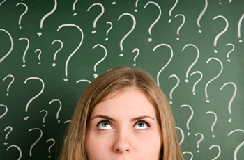A woman looks up at a chalkboard full of question marks.