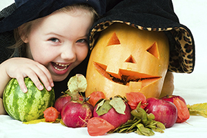 A little girl in a witch costume laughs and poses with her pumpkin.